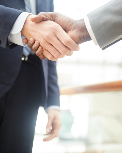 Two people in business suits shaking hands, suggesting agreement or partnership, with a blurred office background.